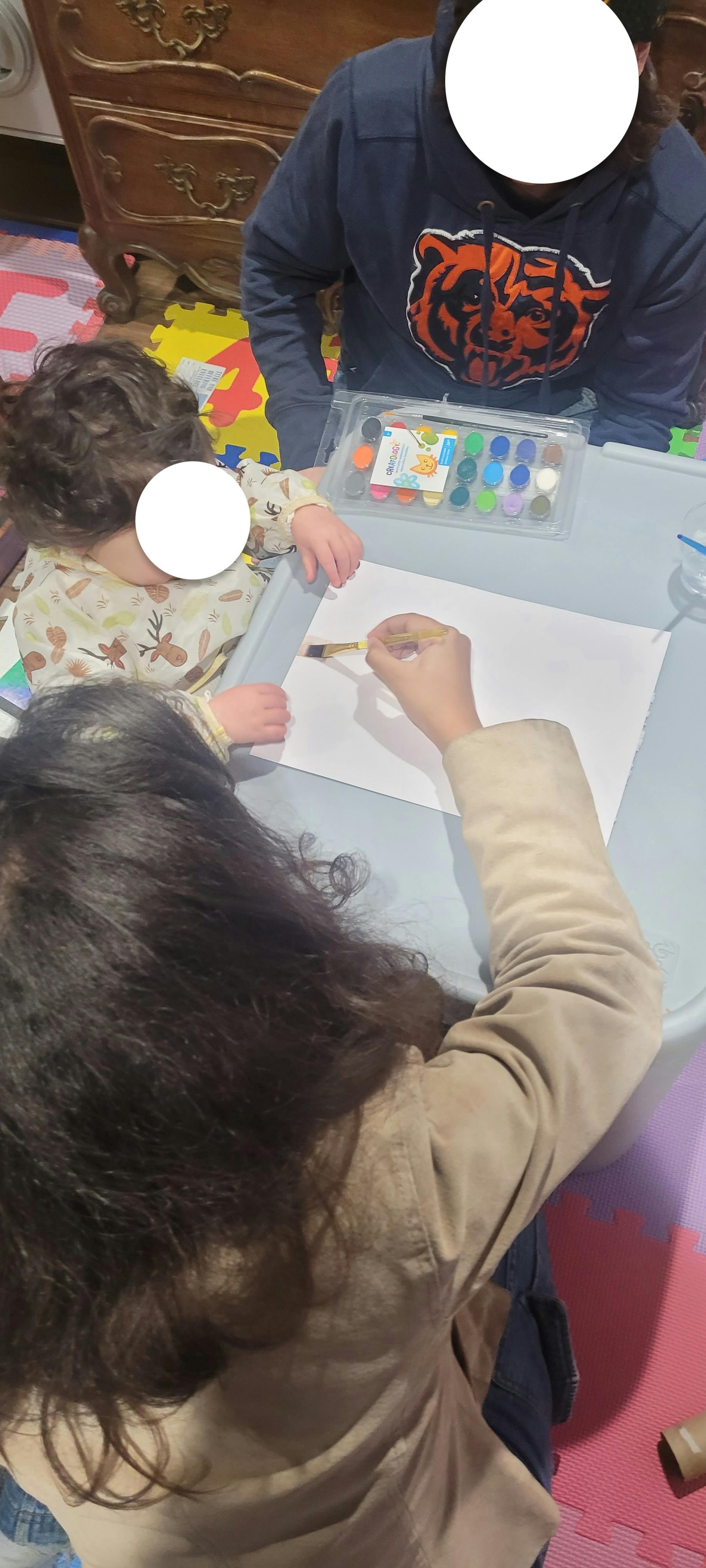 Person painting on paper with a child and another person nearby