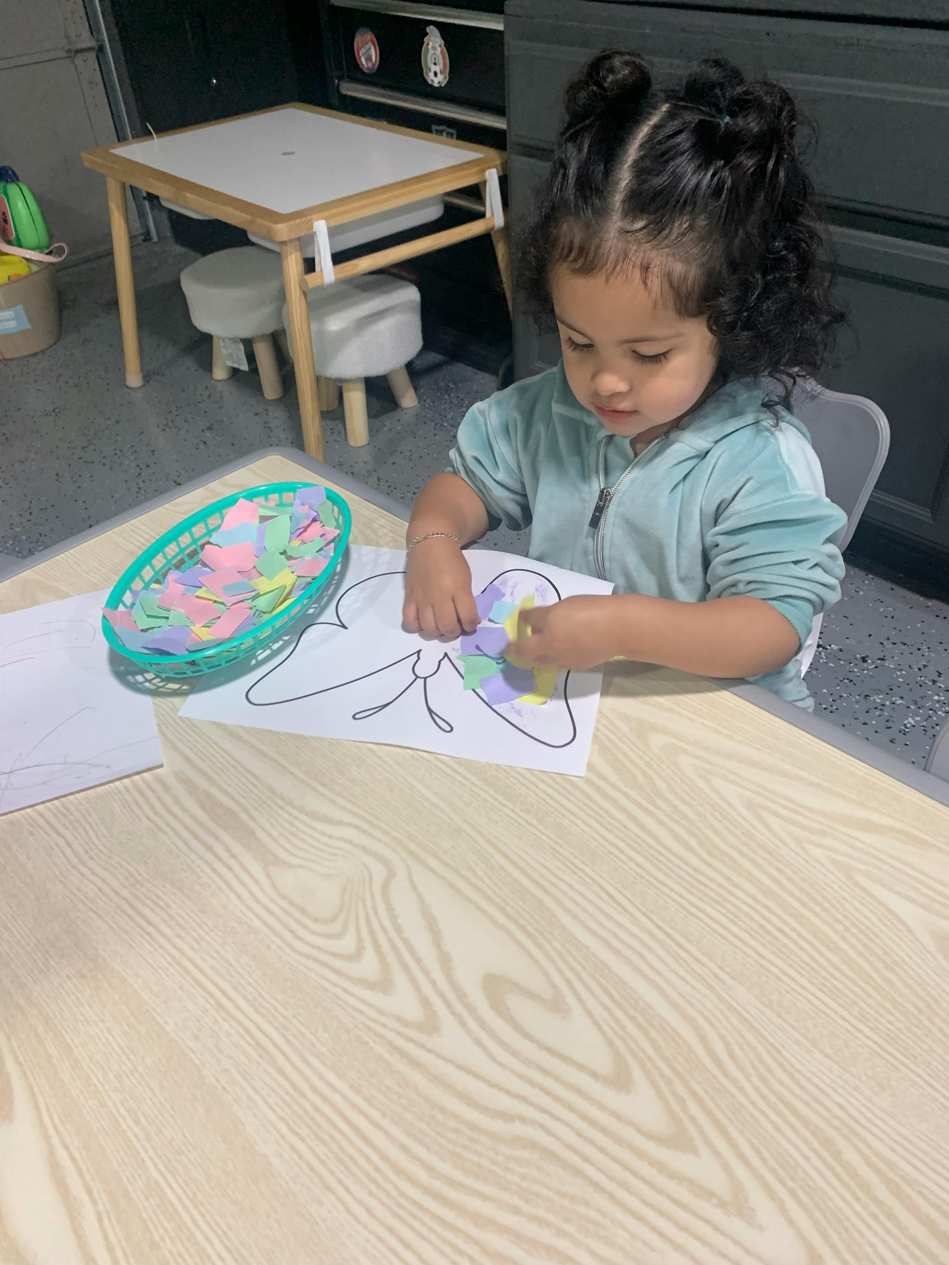Child decorating a butterfly drawing with colorful paper cutouts