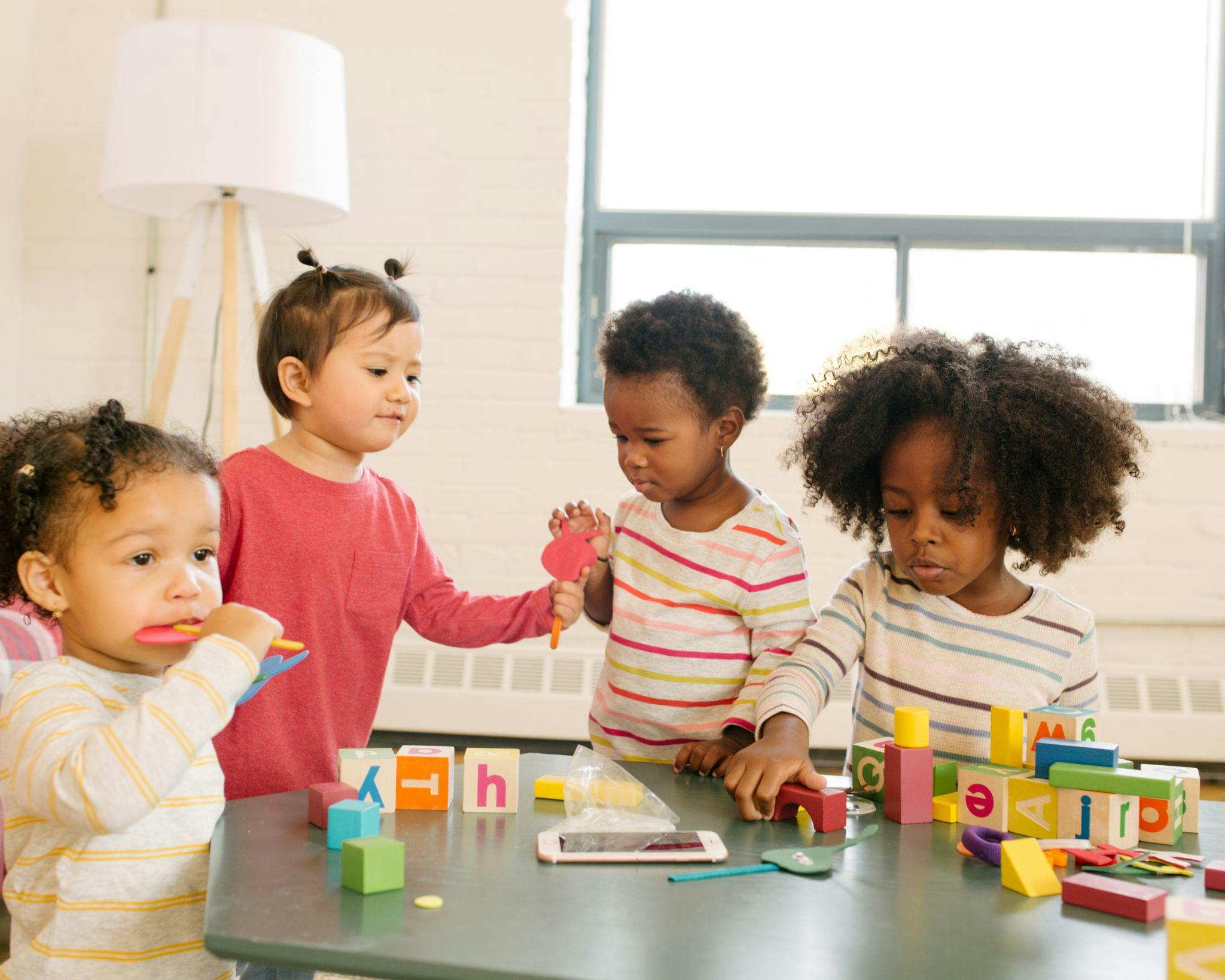 Four children playing with blocks and toys at a table