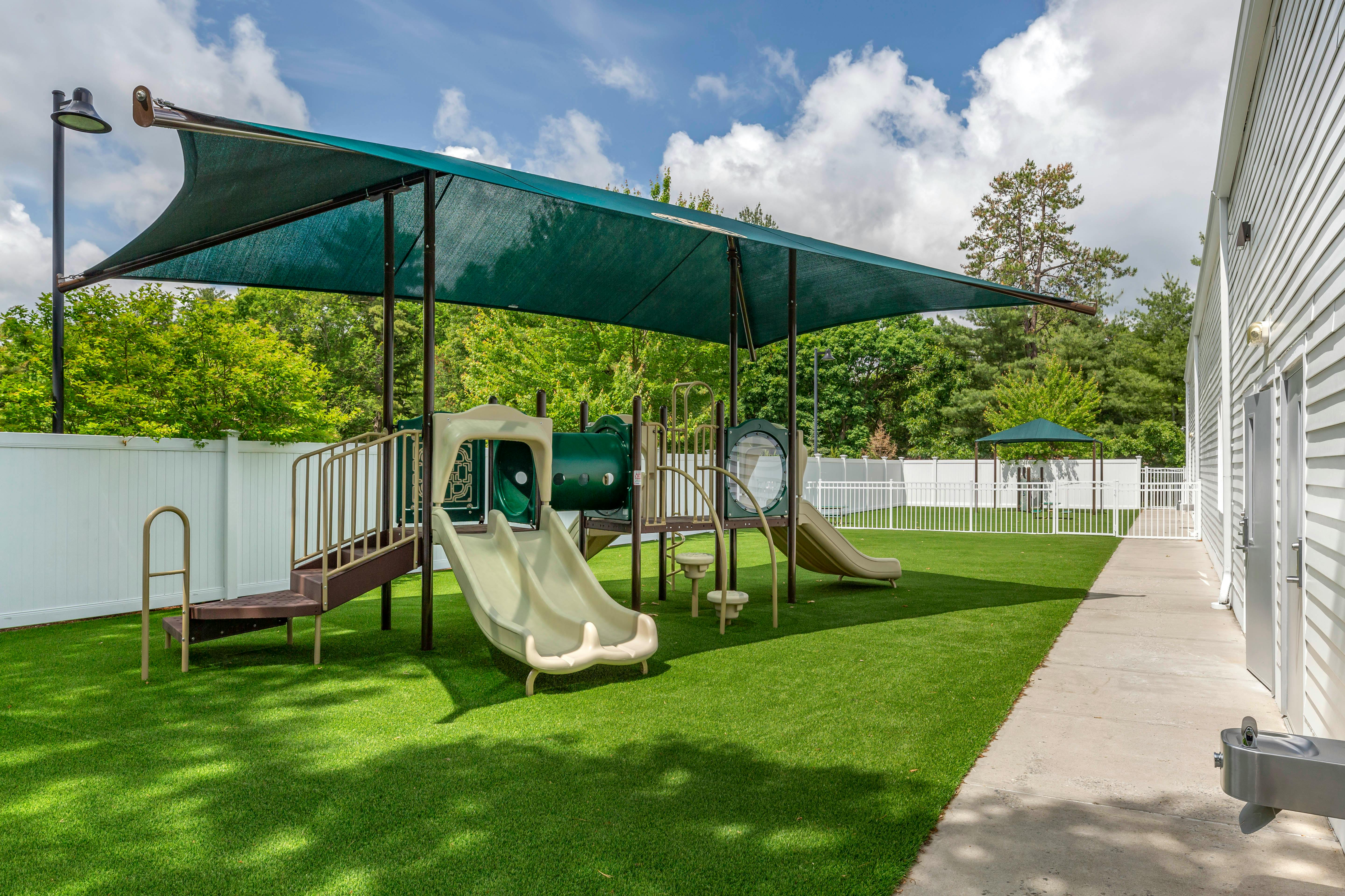 Playground with green turf, slides, climbing structures, and a shade canopy