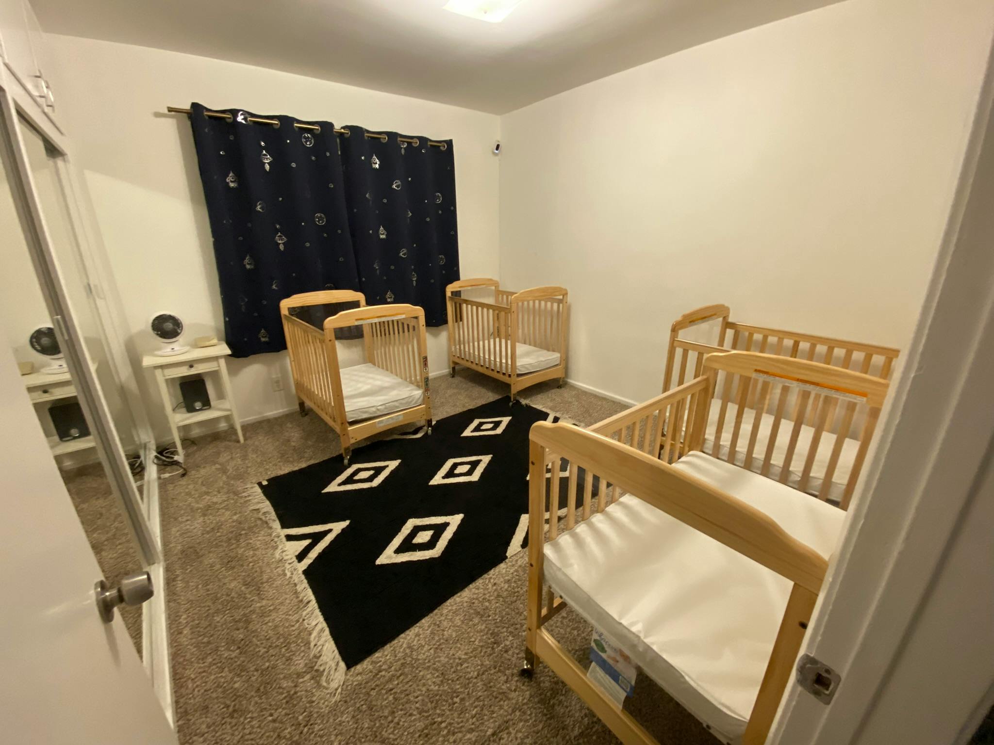 Room with multiple wooden cribs and a black and white rug