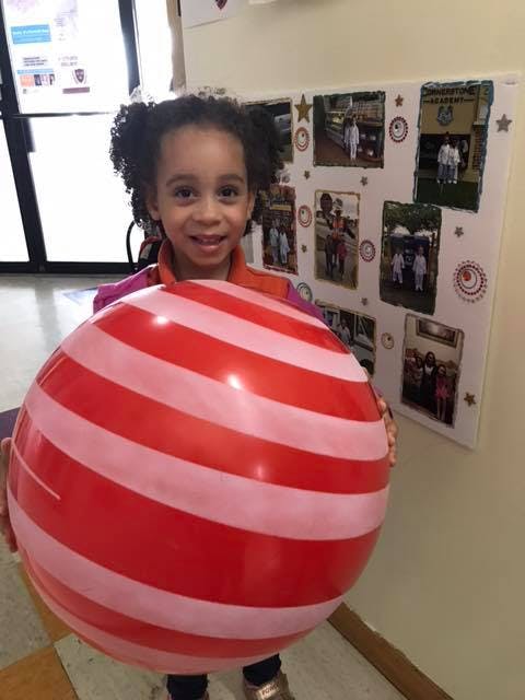 Child holding a large red and pink striped ball