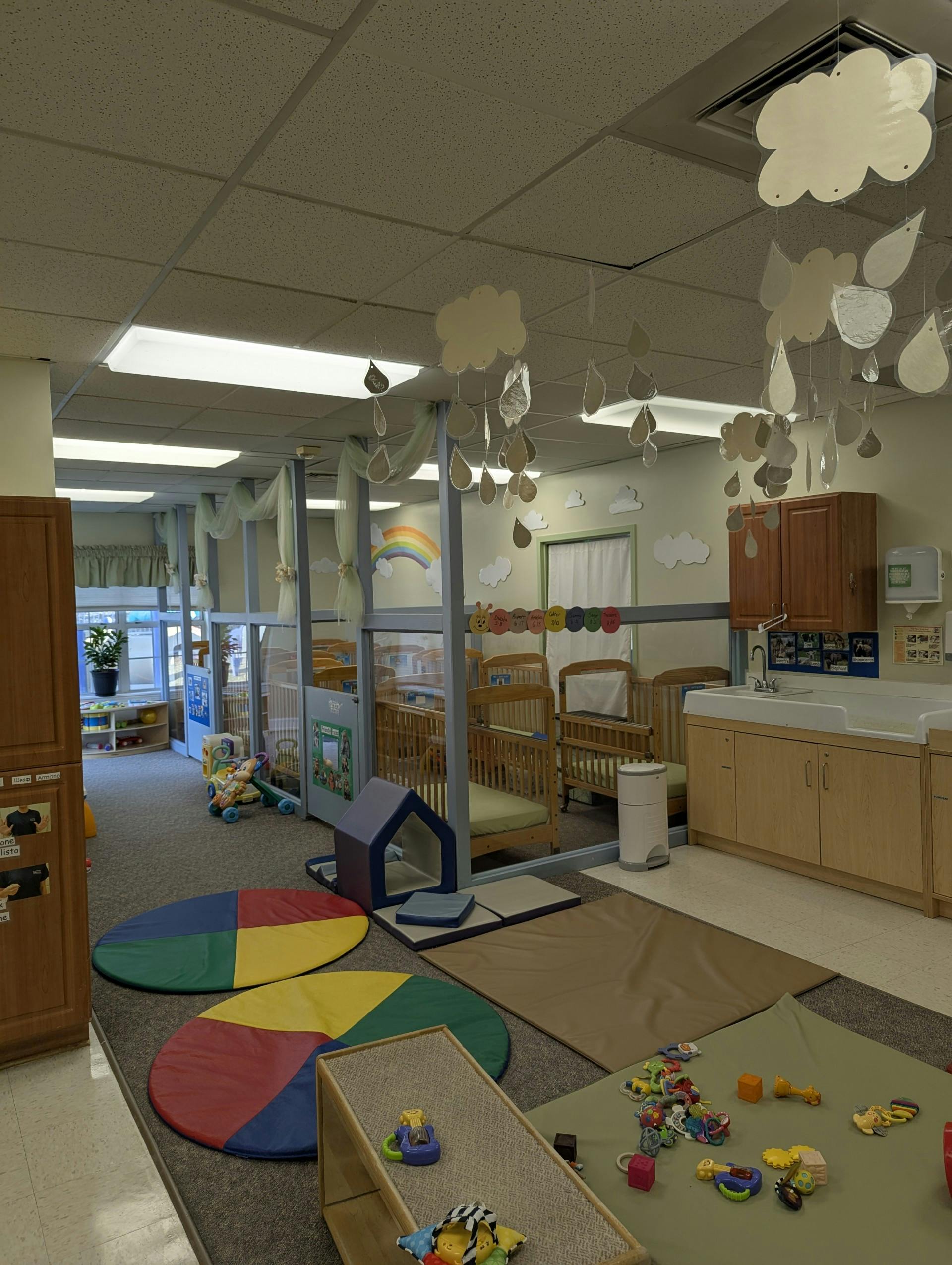 A colorful childcare room with cribs, play mats, and baby toys