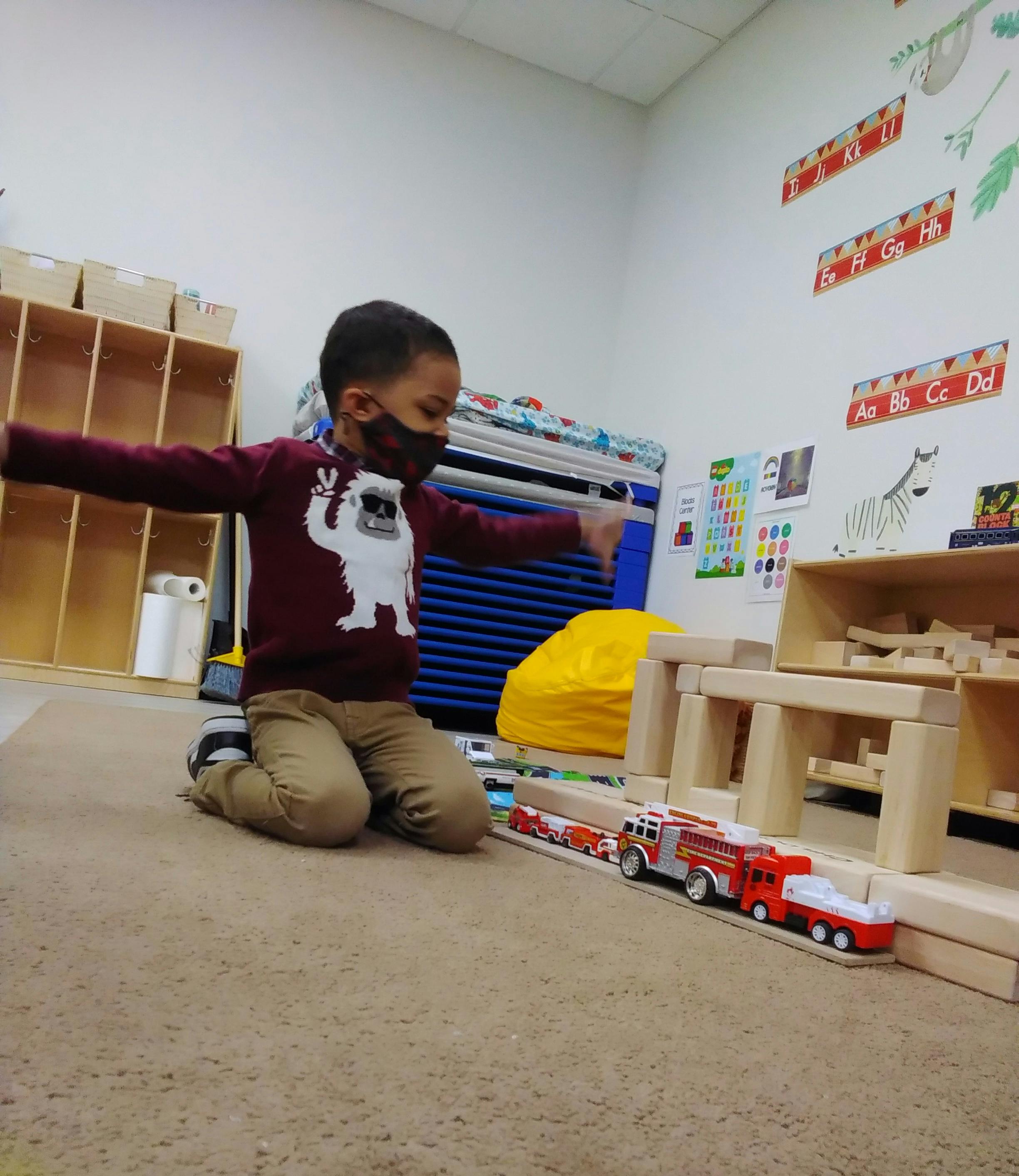 Child in a mask playing with toy trucks on the floor