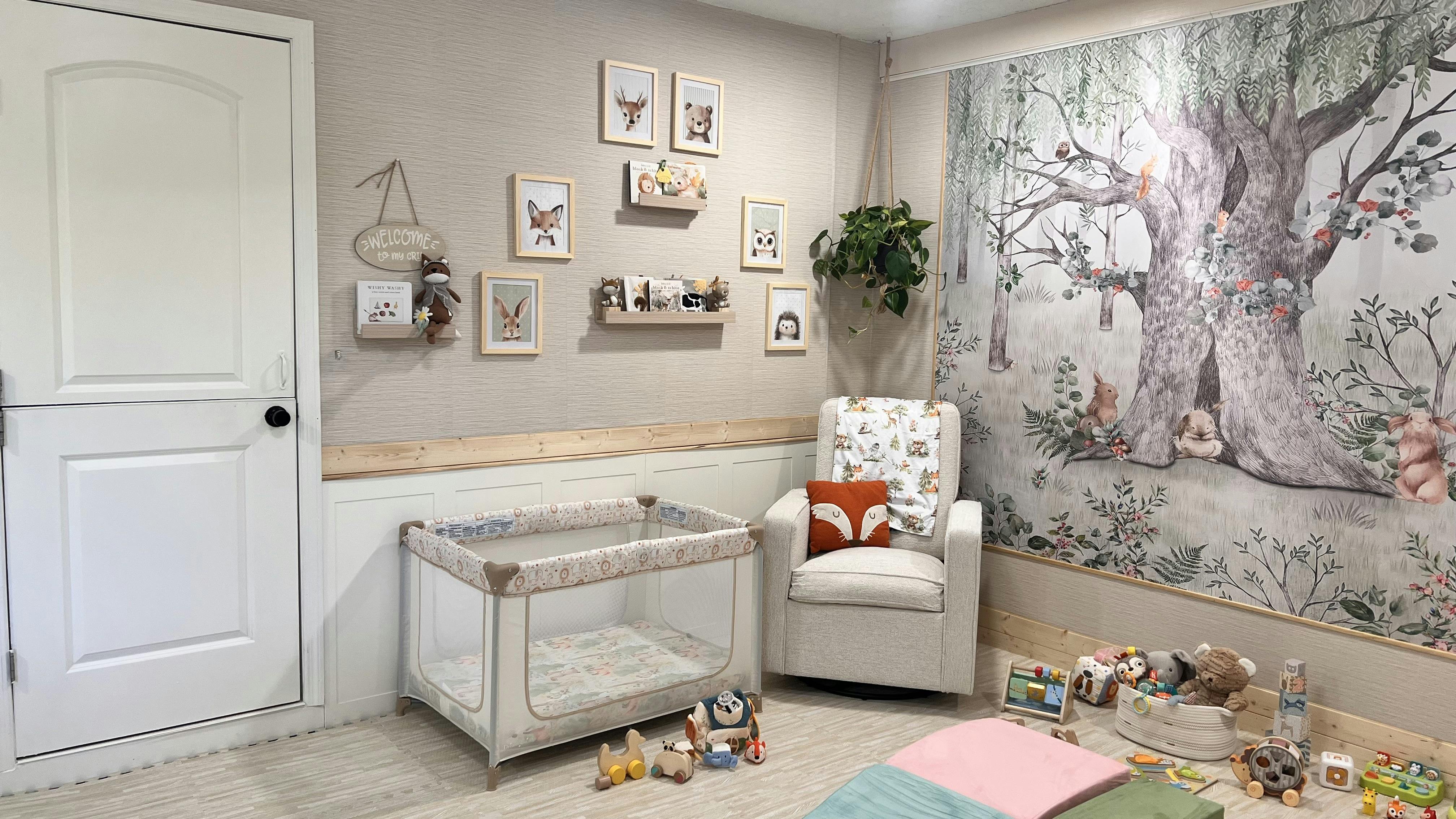 Nursery room with a crib, armchair, and forest-themed wall mural