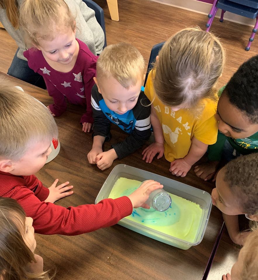Children gathered around a table, one child pouring liquid into a tray
