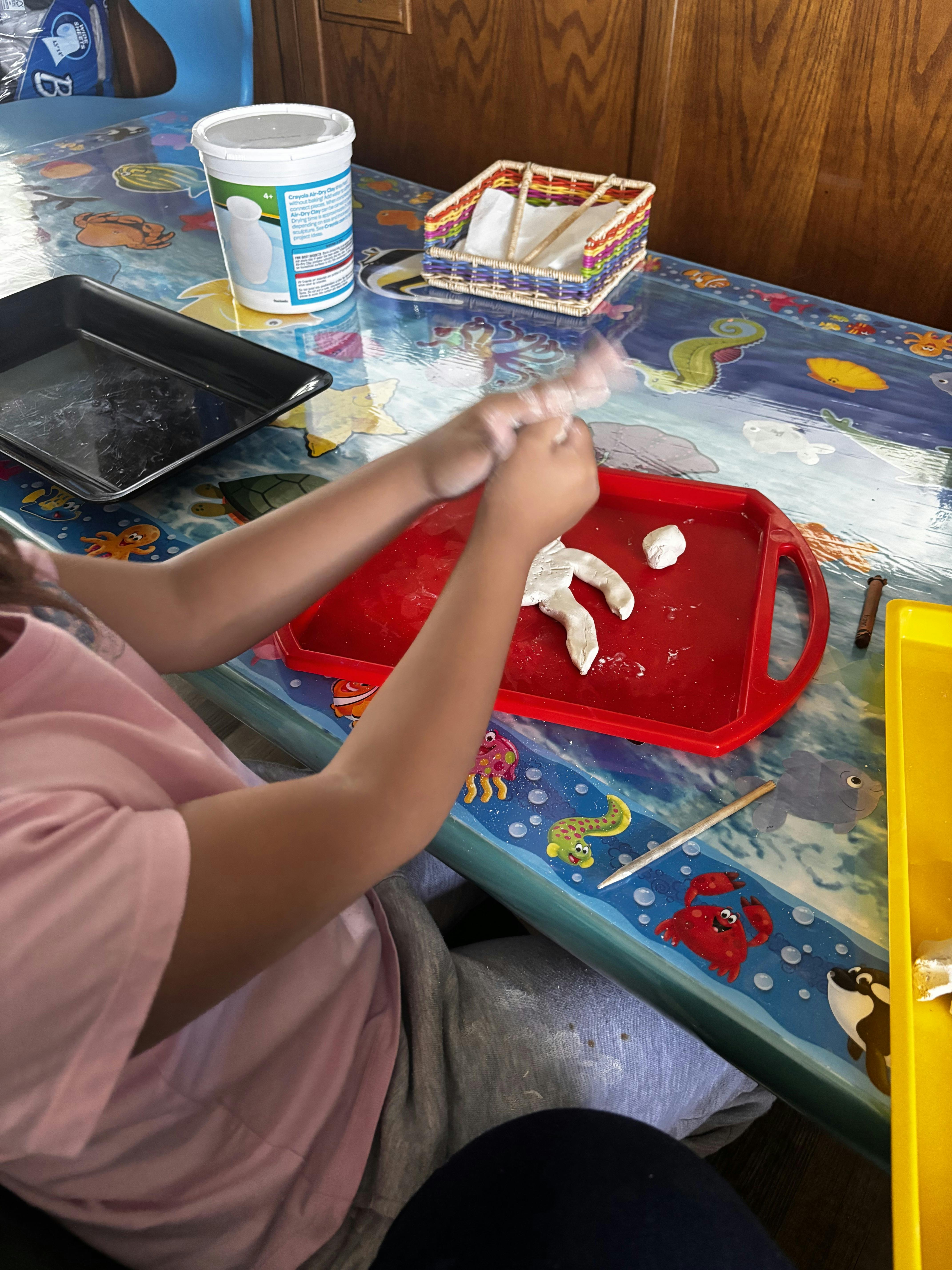 Child molding clay on a red tray