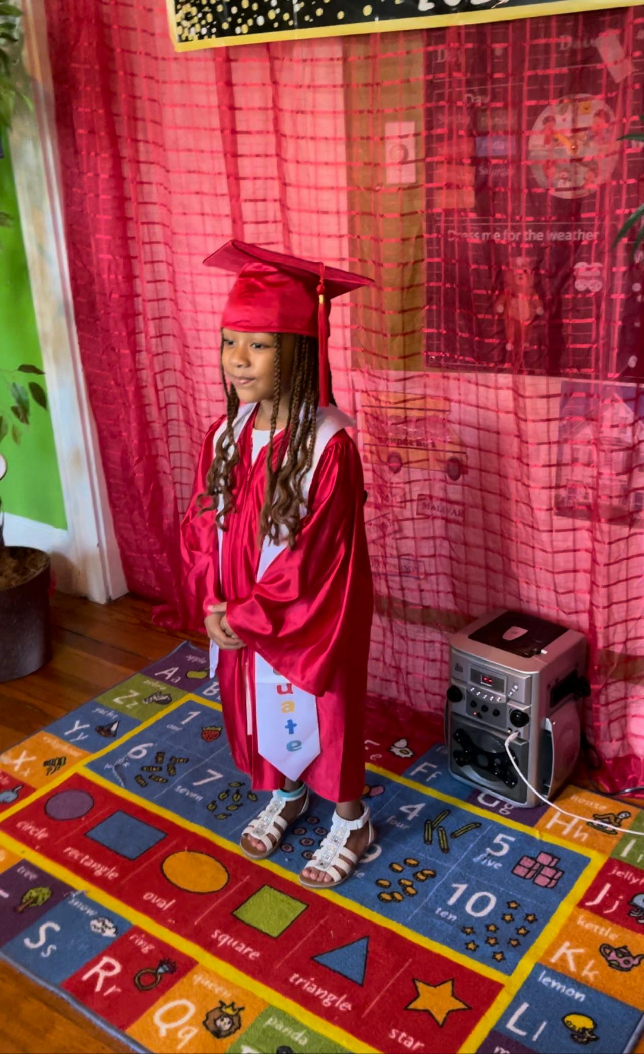 Child in a red graduation cap and gown standing on a colorful rug