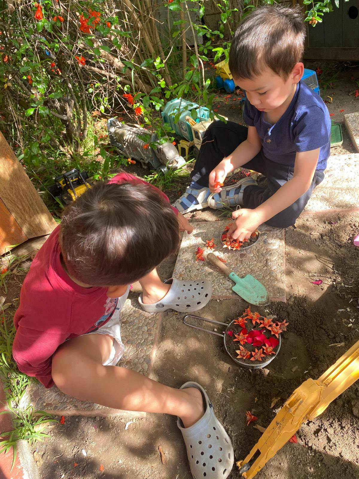 Two children playing in dirt, putting flowers in a small pot