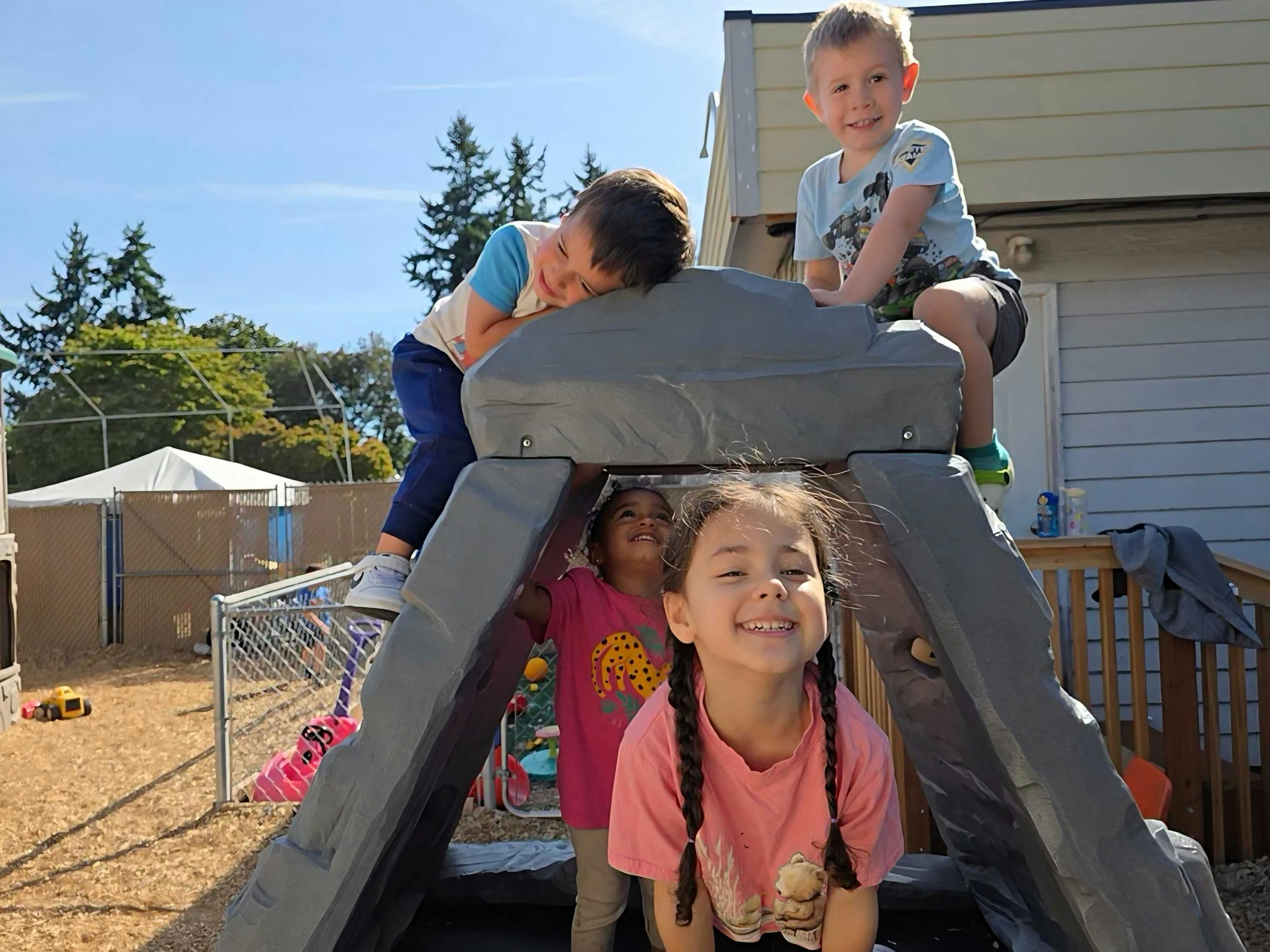 Four children playing on and inside a plastic climbing structure outdoors