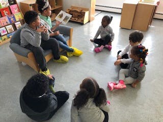 Children sitting on floor and chair reading a book in a classroom