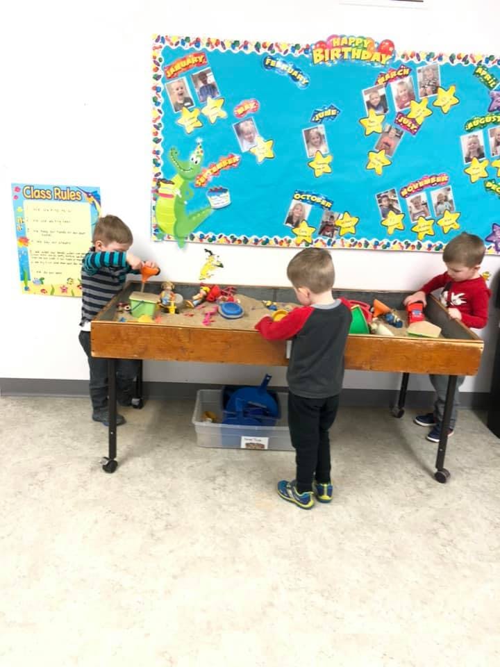 Three children playing at a sand table in a classroom