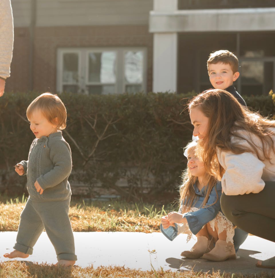 Toddler walking barefoot on a path with other children nearby