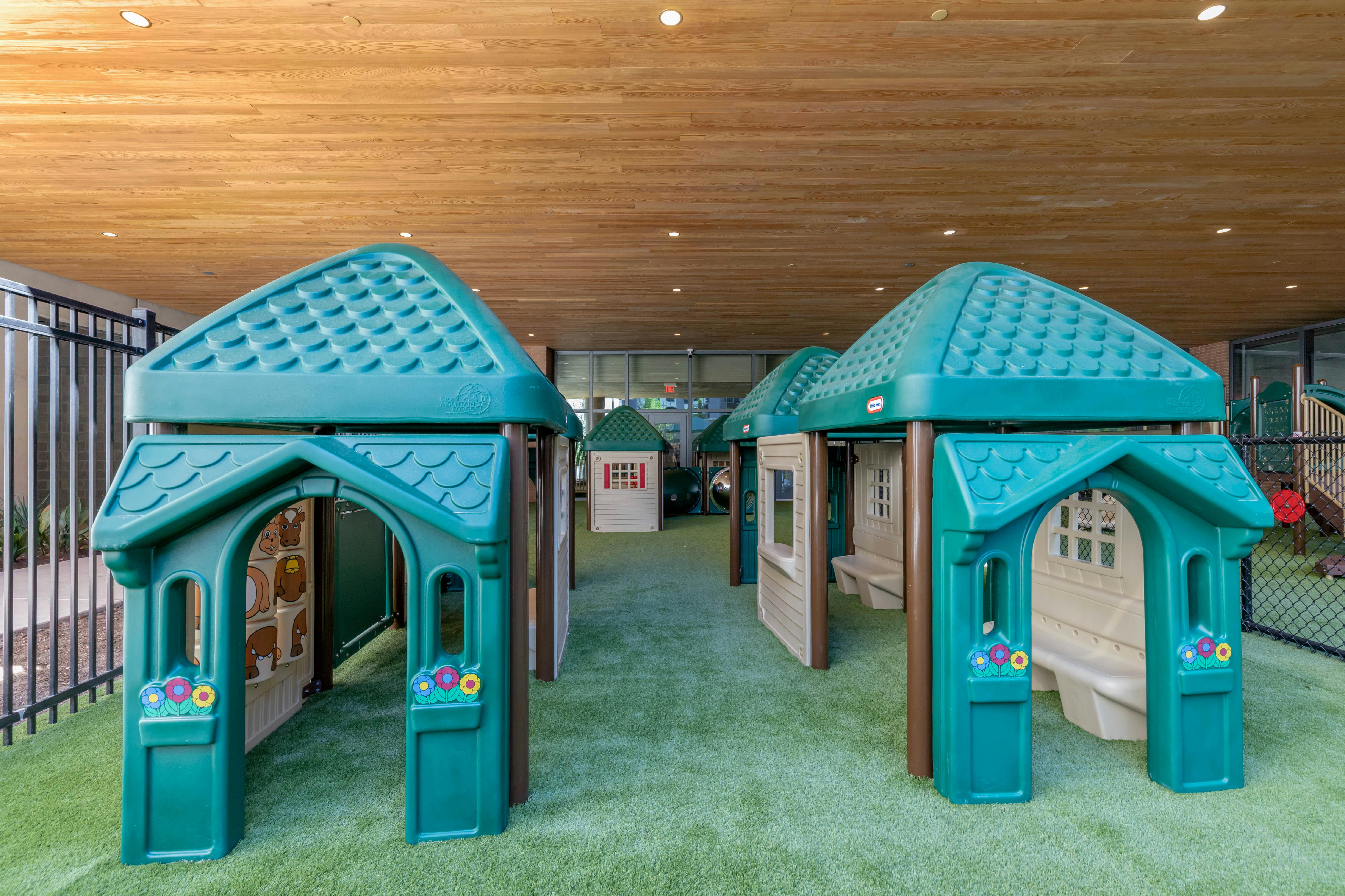 multiple green and brown plastic playhouses on artificial turf under a wooden ceiling