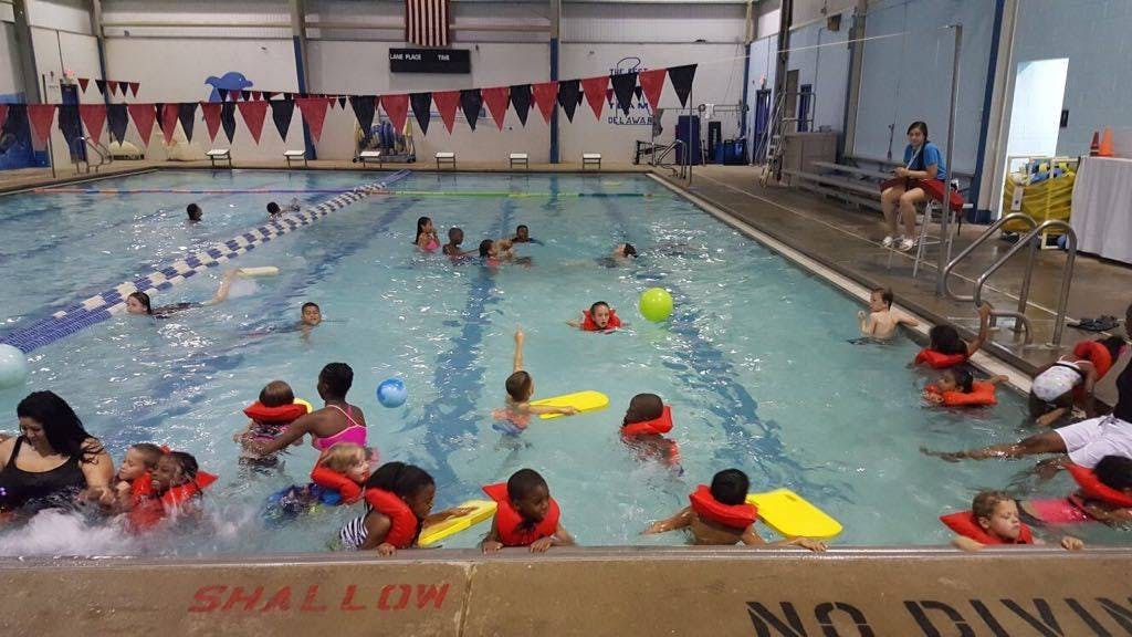 People and children in a swimming pool, some wearing life vests