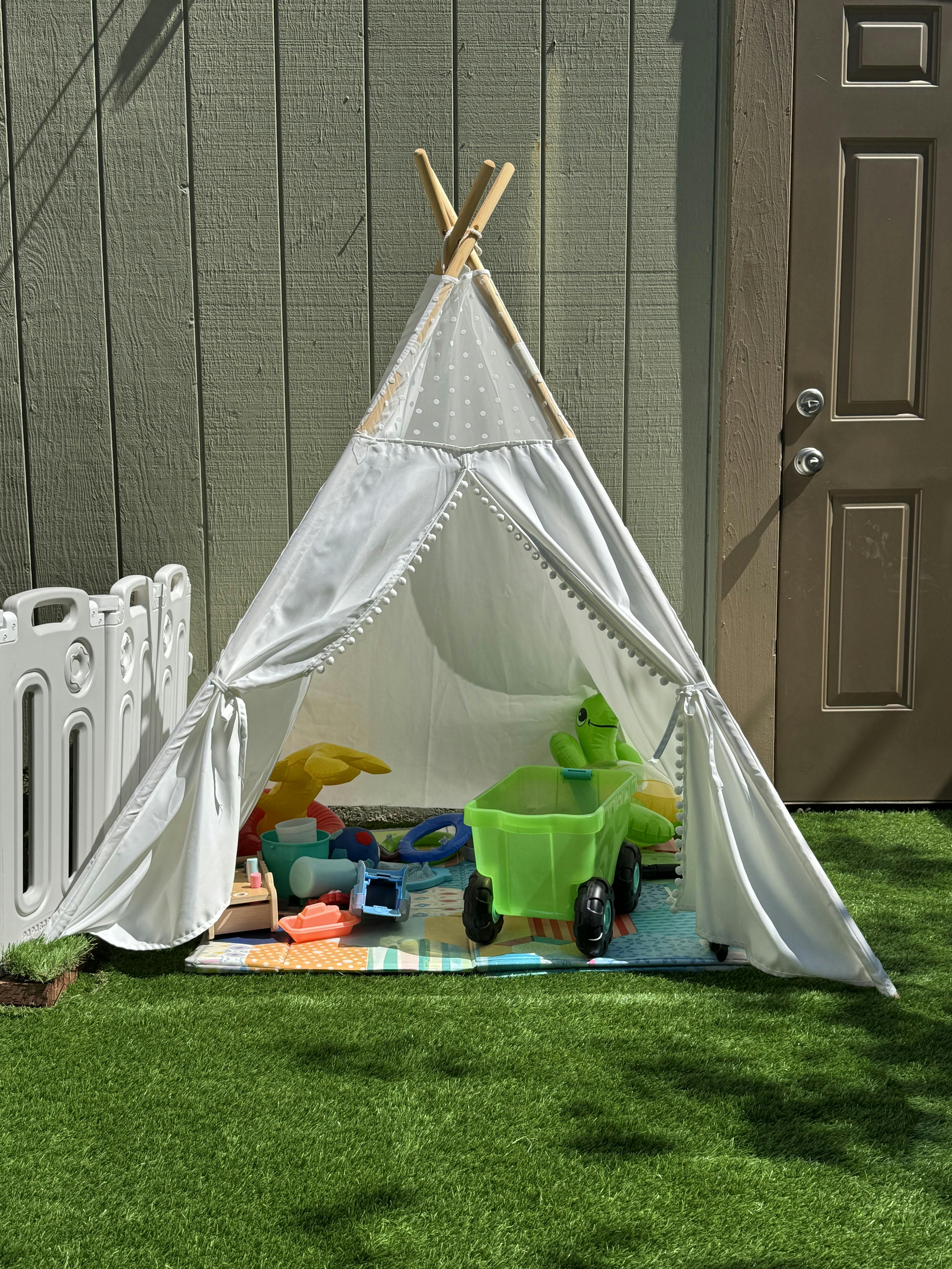 White teepee tent with toys inside on a green lawn