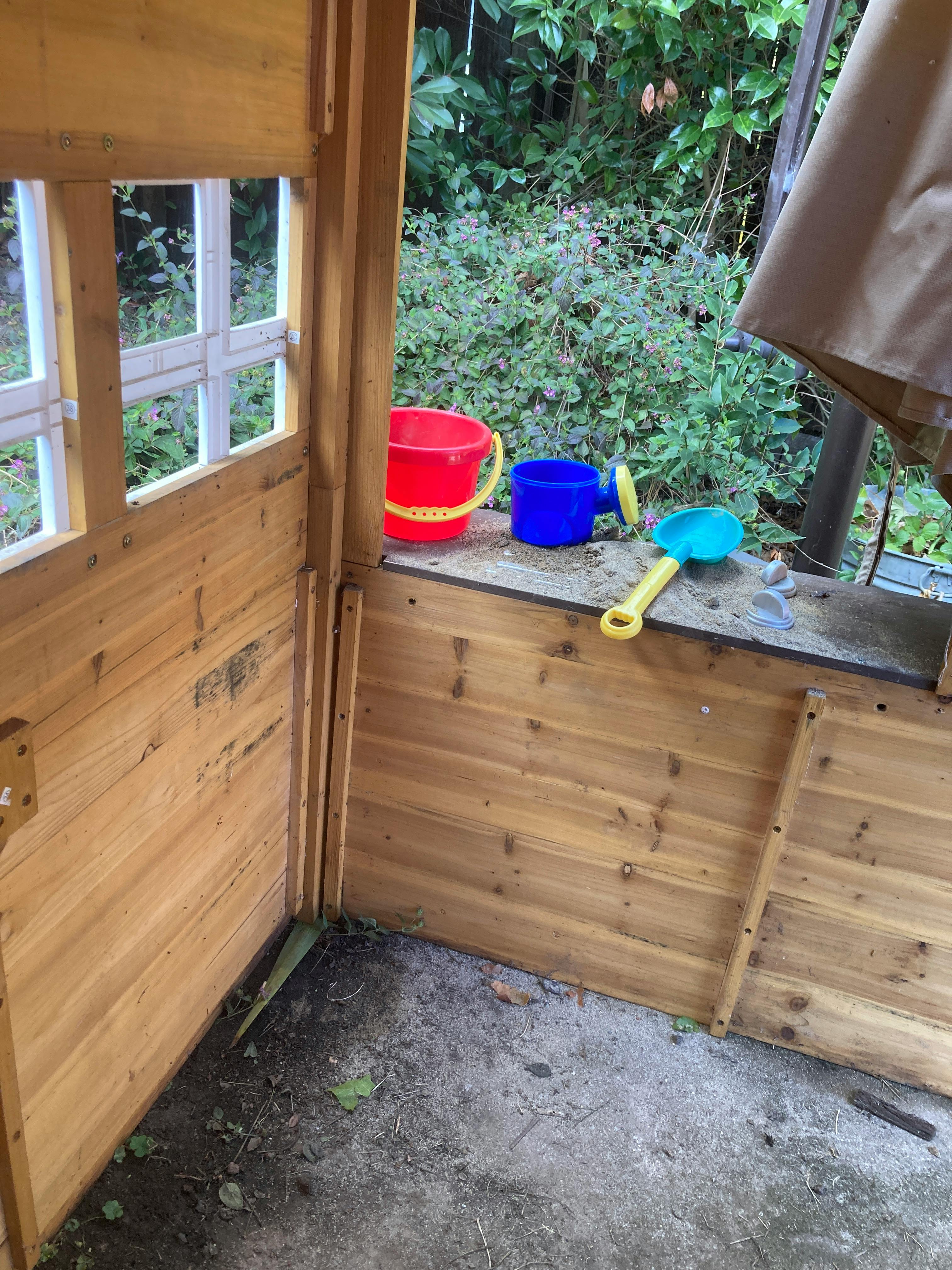 Playhouse interior with a red bucket, blue watering can, and yellow shovel
