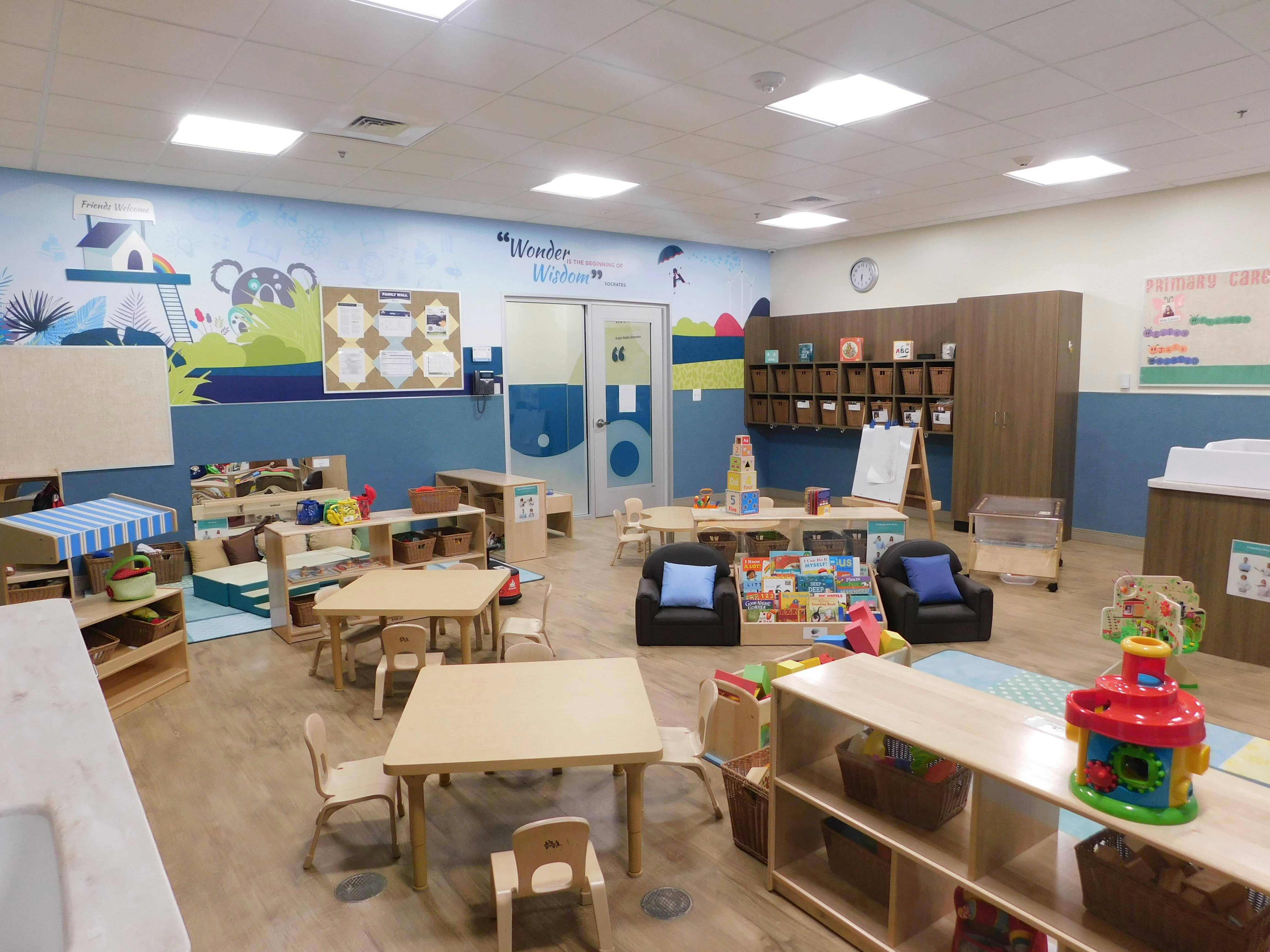 Empty classroom with small tables and chairs, toys, and colorful wall murals