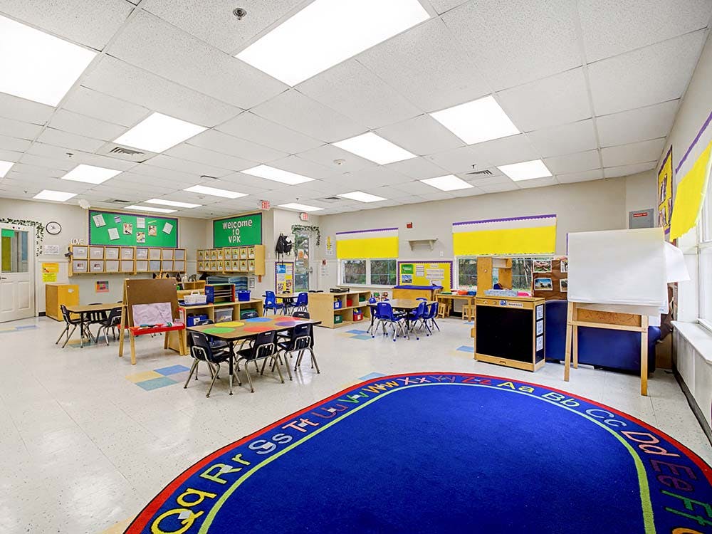 Empty classroom with tables, chairs, and a blue rug with alphabet letters
