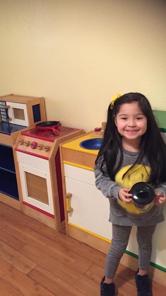 Child holding a toy pot in a play kitchen