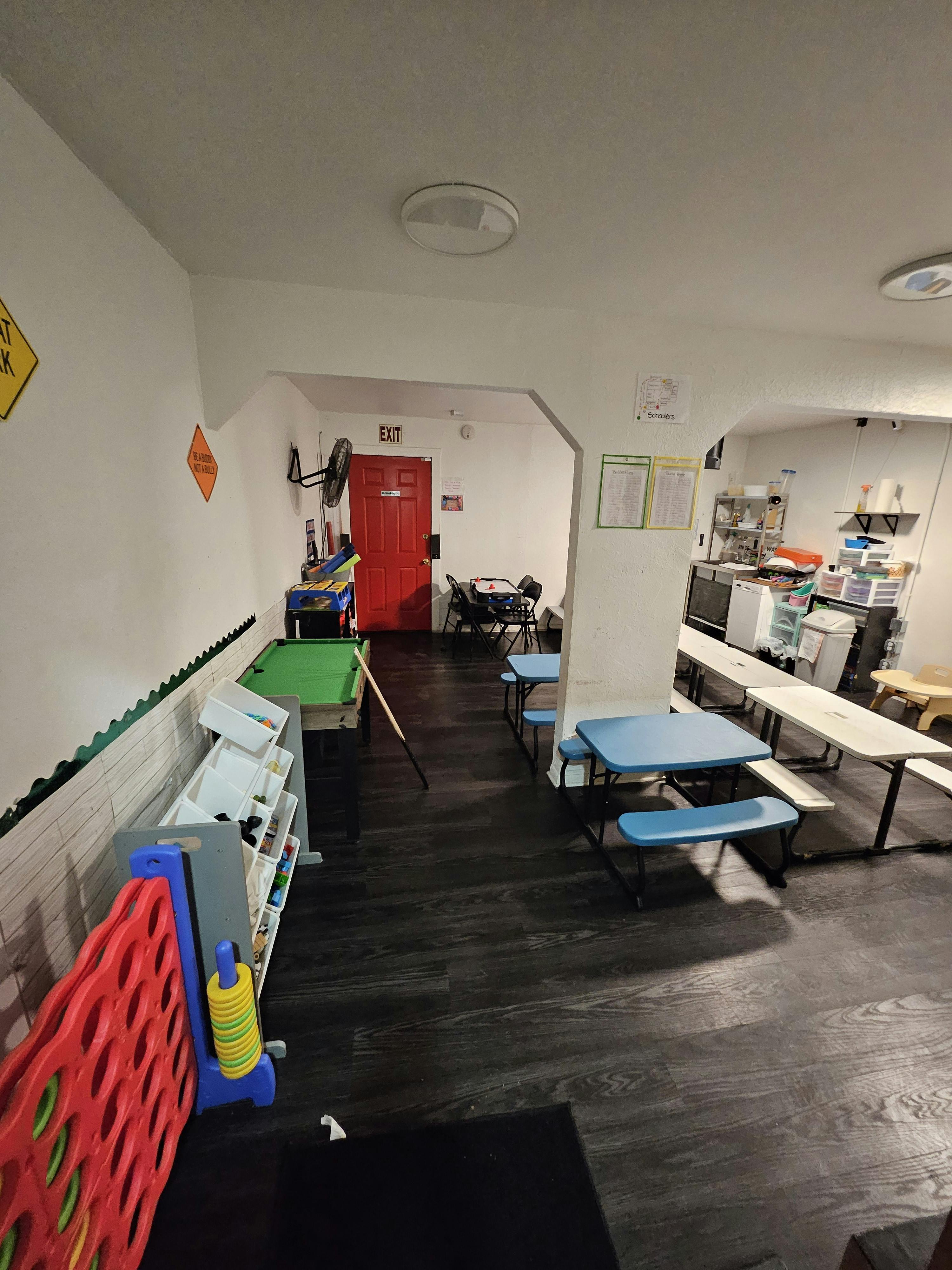 Room with a pool table, red exit door, and blue picnic tables