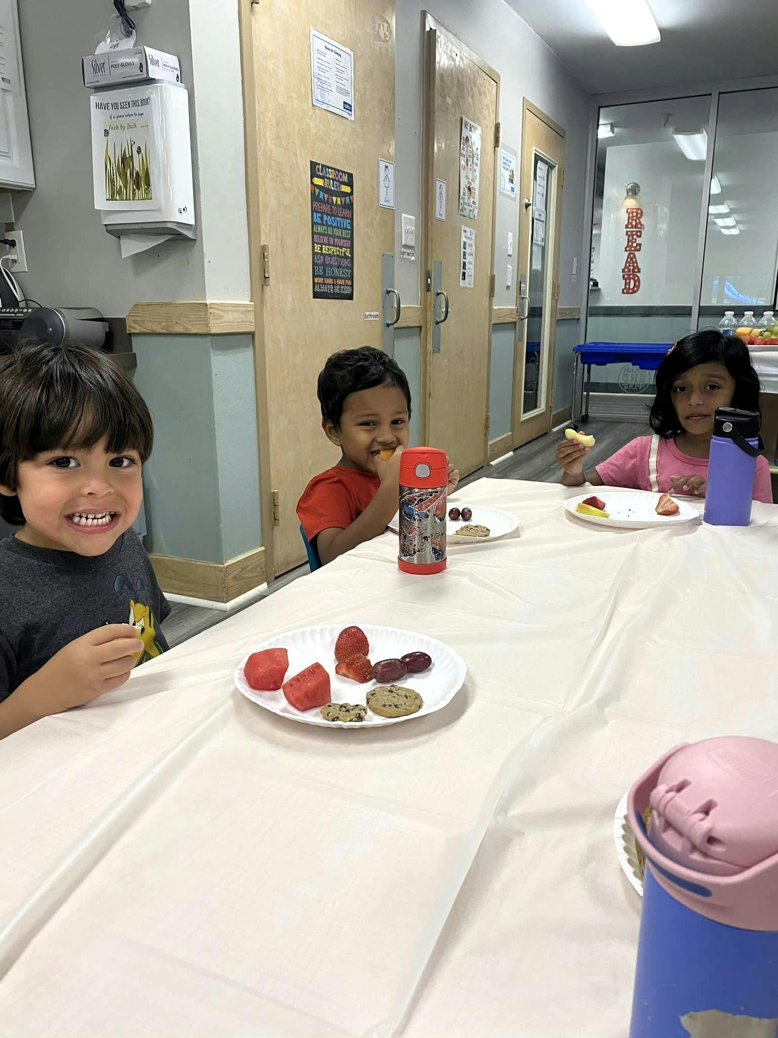 Three children sitting at a table with plates of food