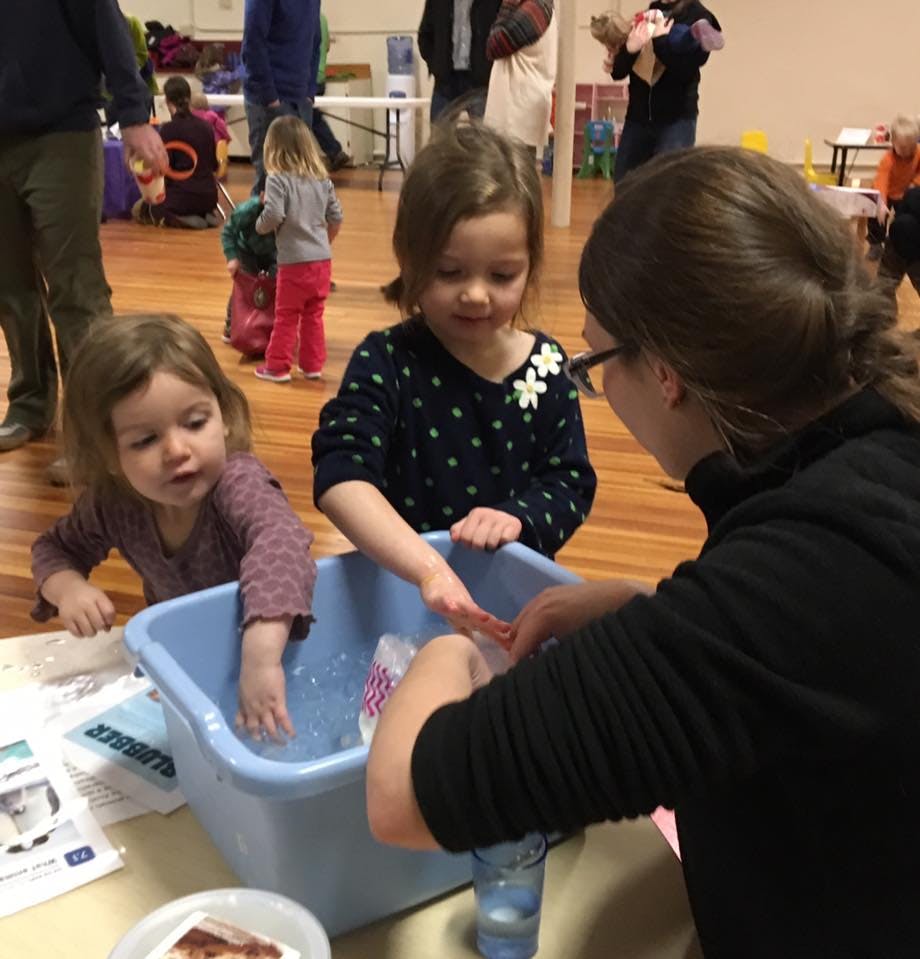 Two children and an adult washing items in a blue tub