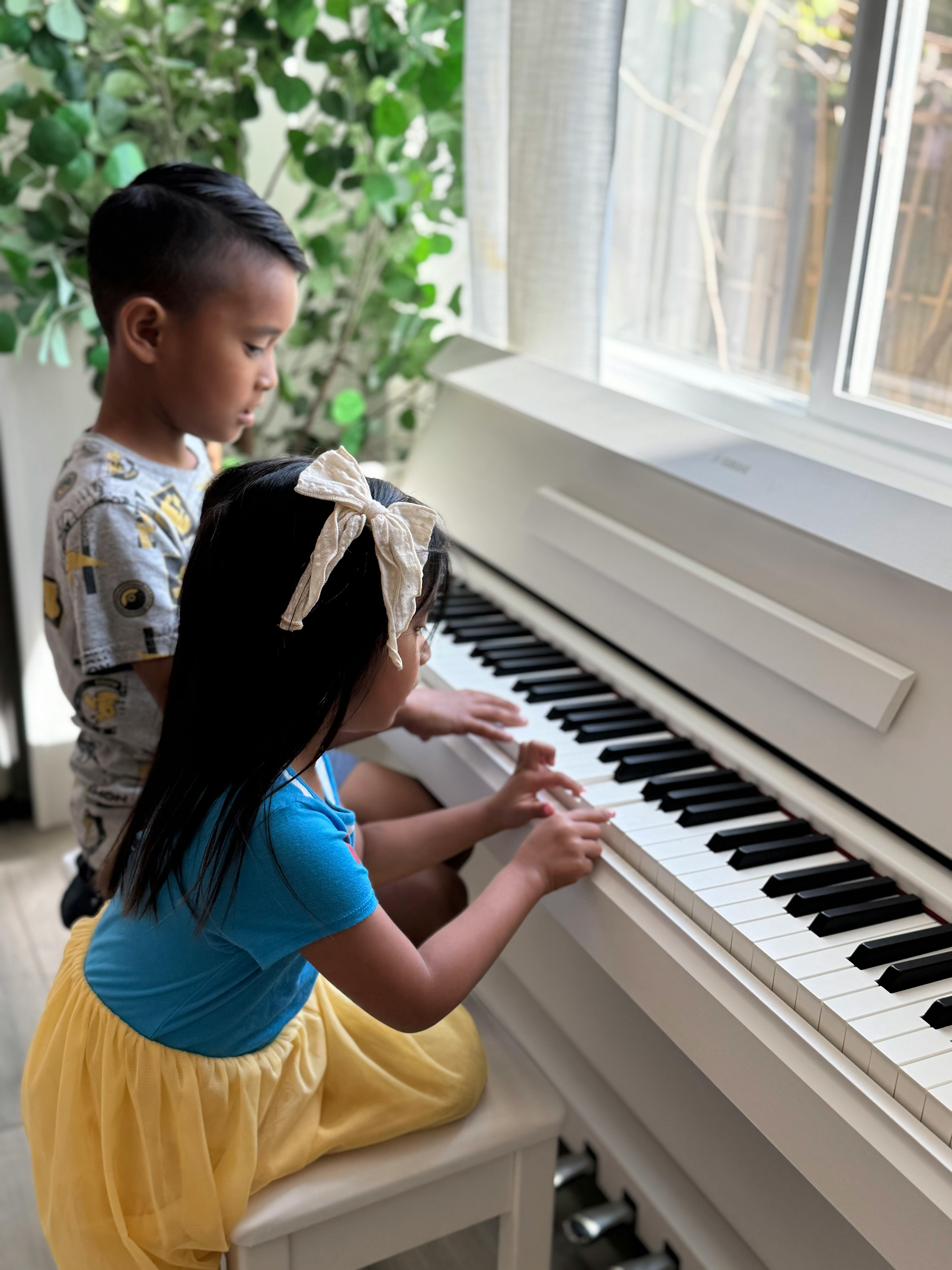 Two children playing a white piano
