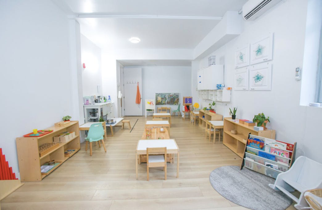 Classroom with small tables and chairs, shelves with learning materials