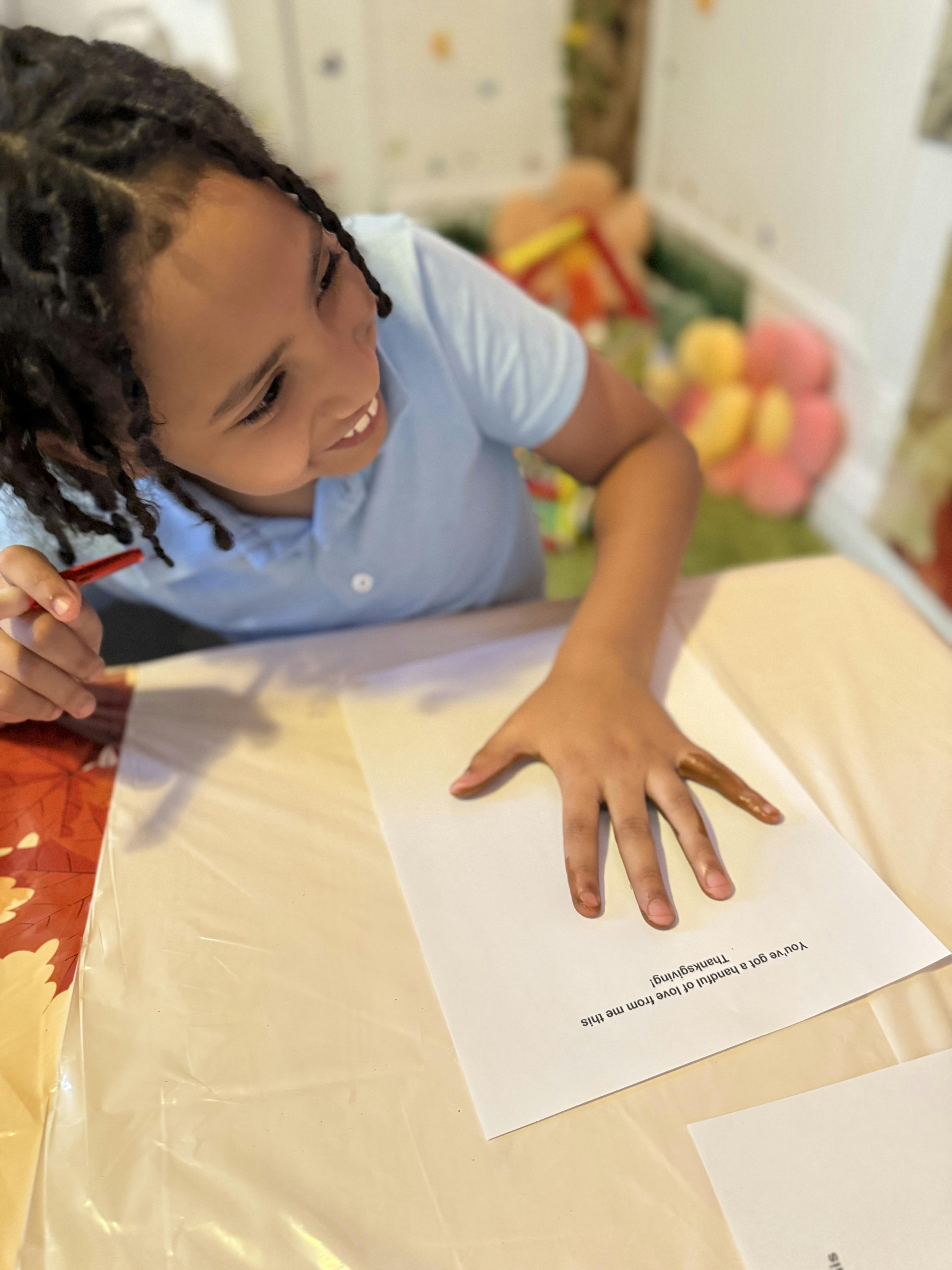 Child smiling while making a handprint turkey craft for Thanksgiving