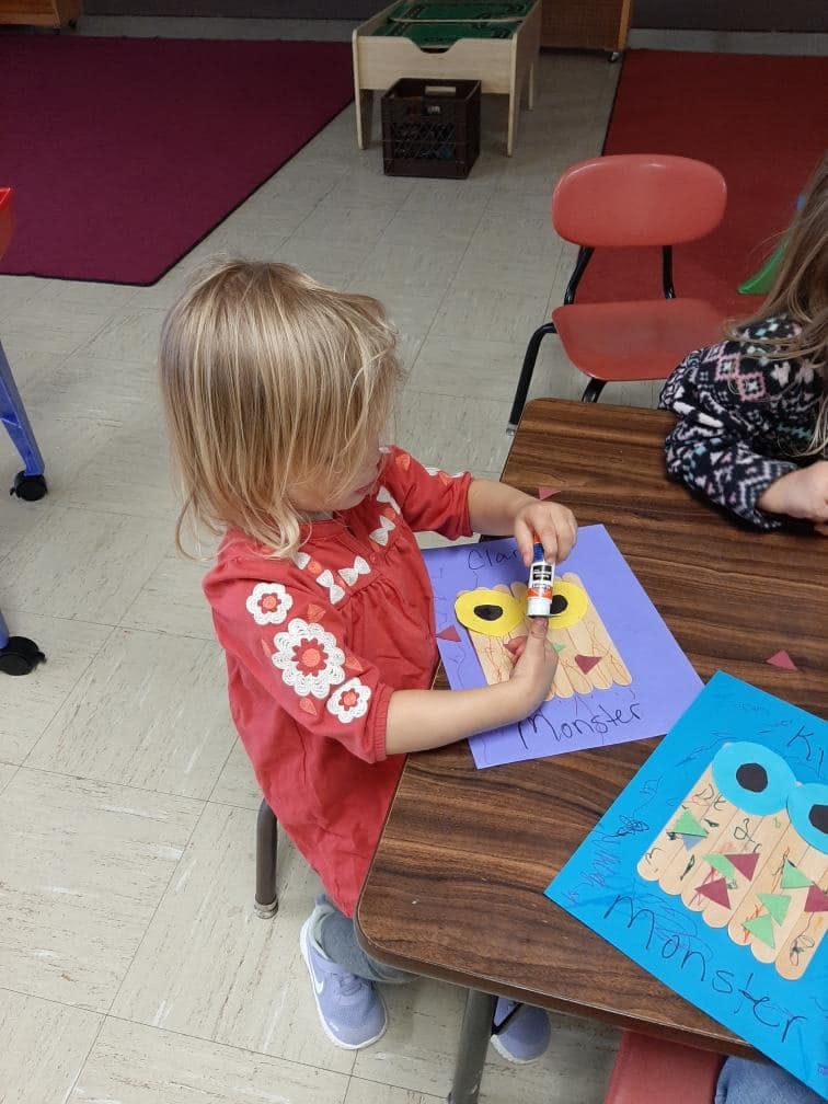 Child gluing craft pieces onto a paper monster