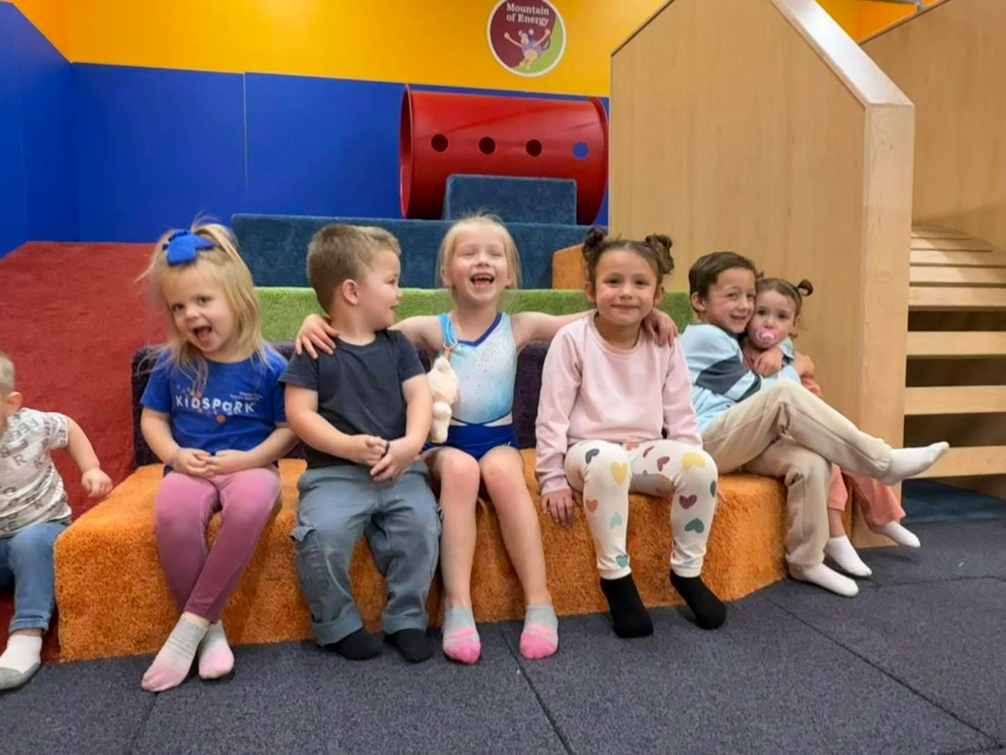 Group of children sitting on a padded bench in an indoor play area