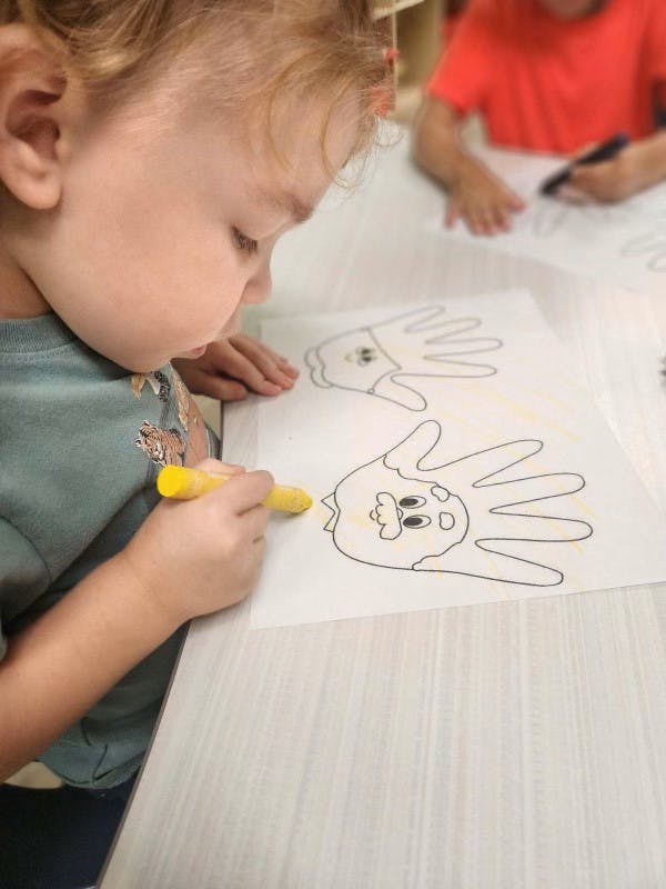Child coloring a handprint drawing with a yellow crayon