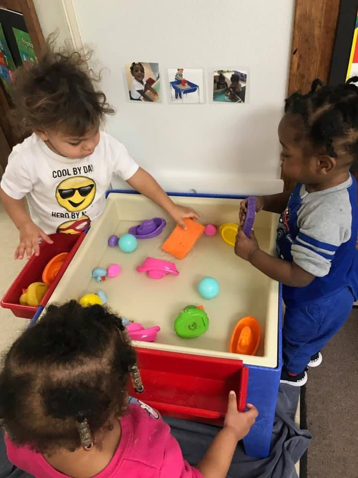 Three children playing with toys in a water table