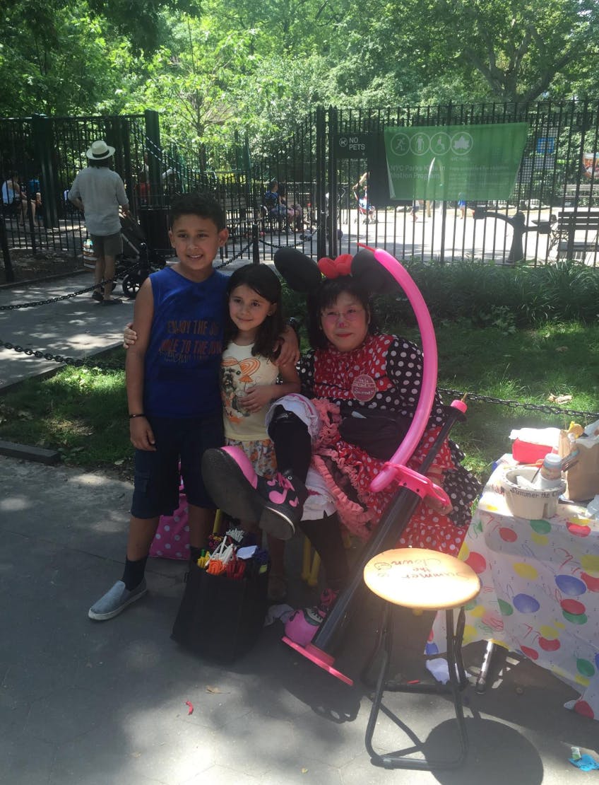 Three children posing outdoors, one in a polka dot dress with a balloon animal