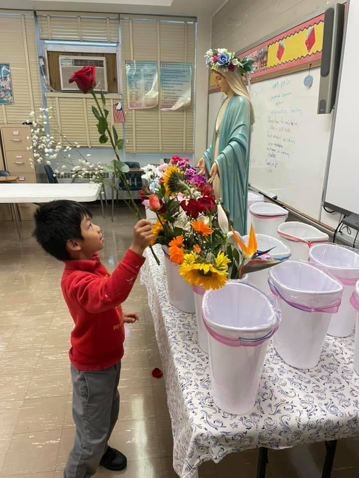 Child placing a red rose into a vase of flowers next to a statue