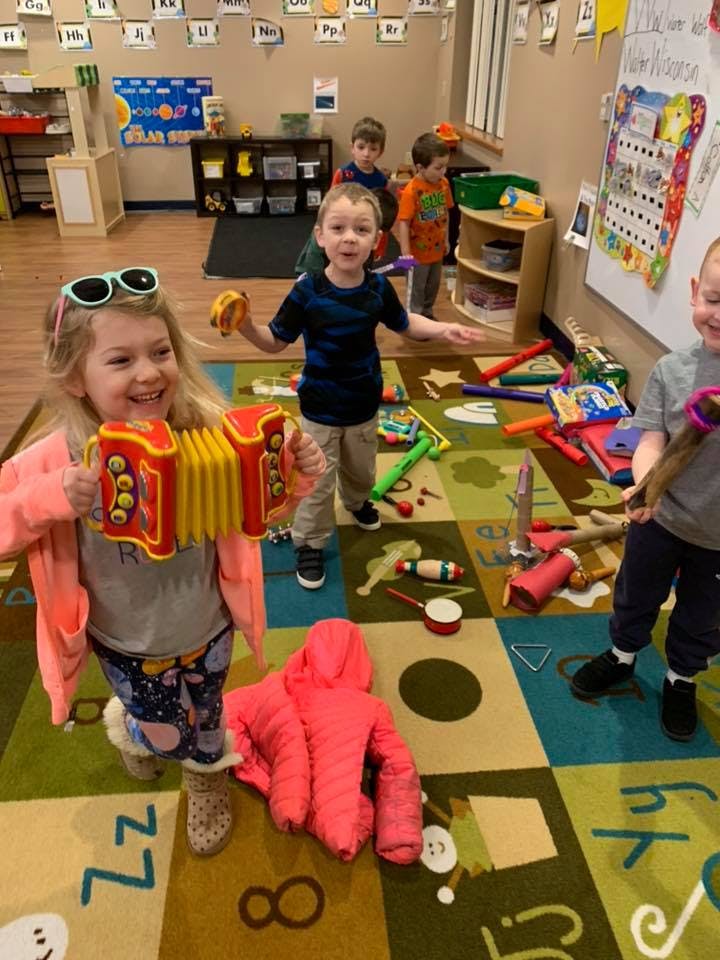 Child playing an accordion toy in a classroom with other children