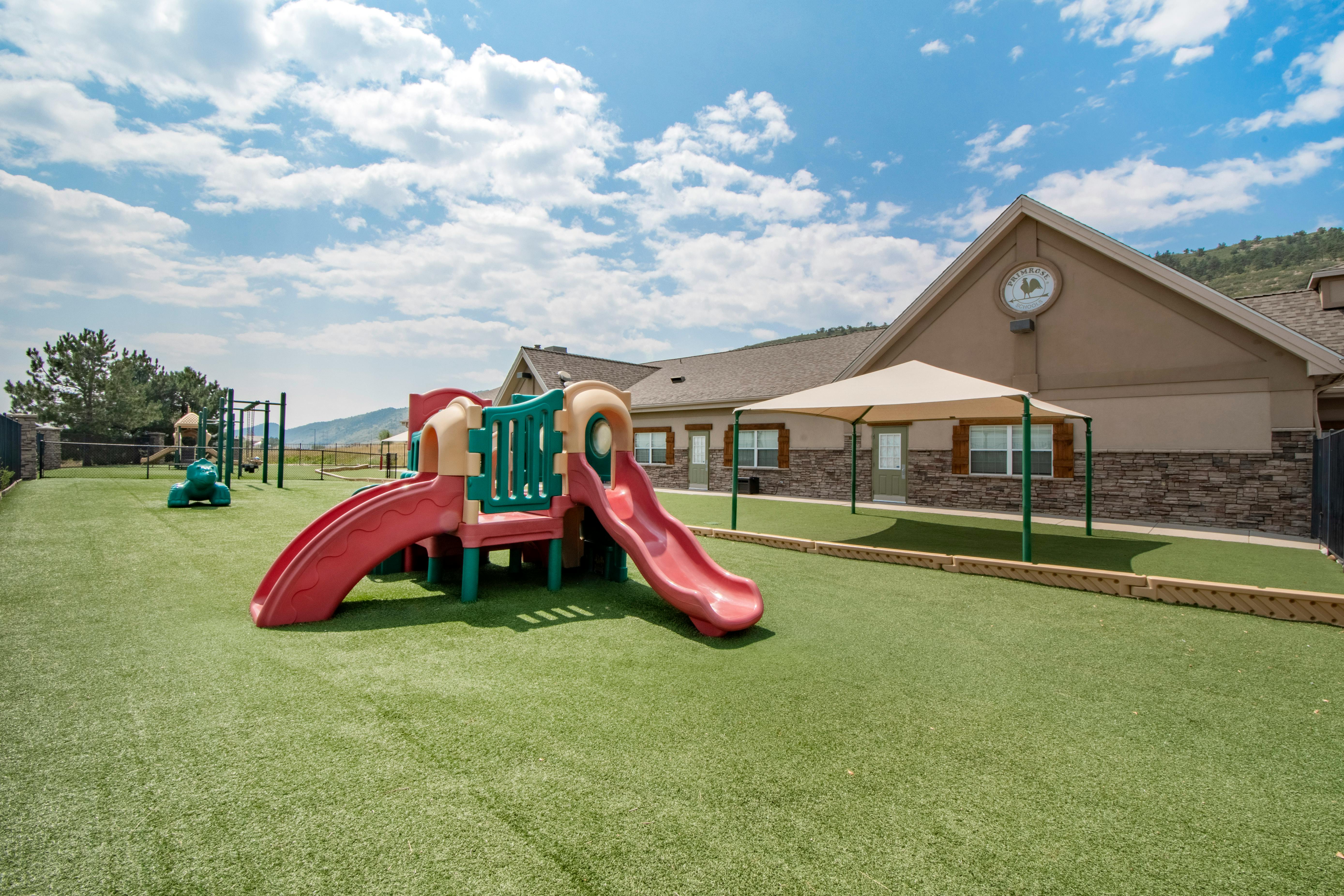 A colorful playground with slides and swings on artificial grass next to a building