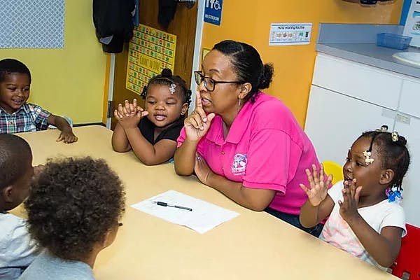 Adult person with glasses talking to children at a table