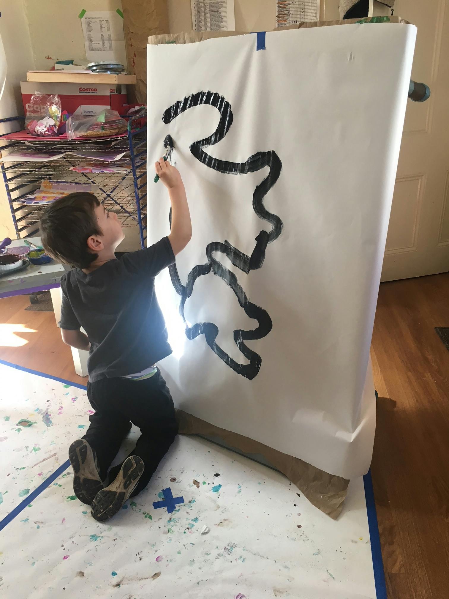 Child kneeling and drawing on a large white paper with black marker
