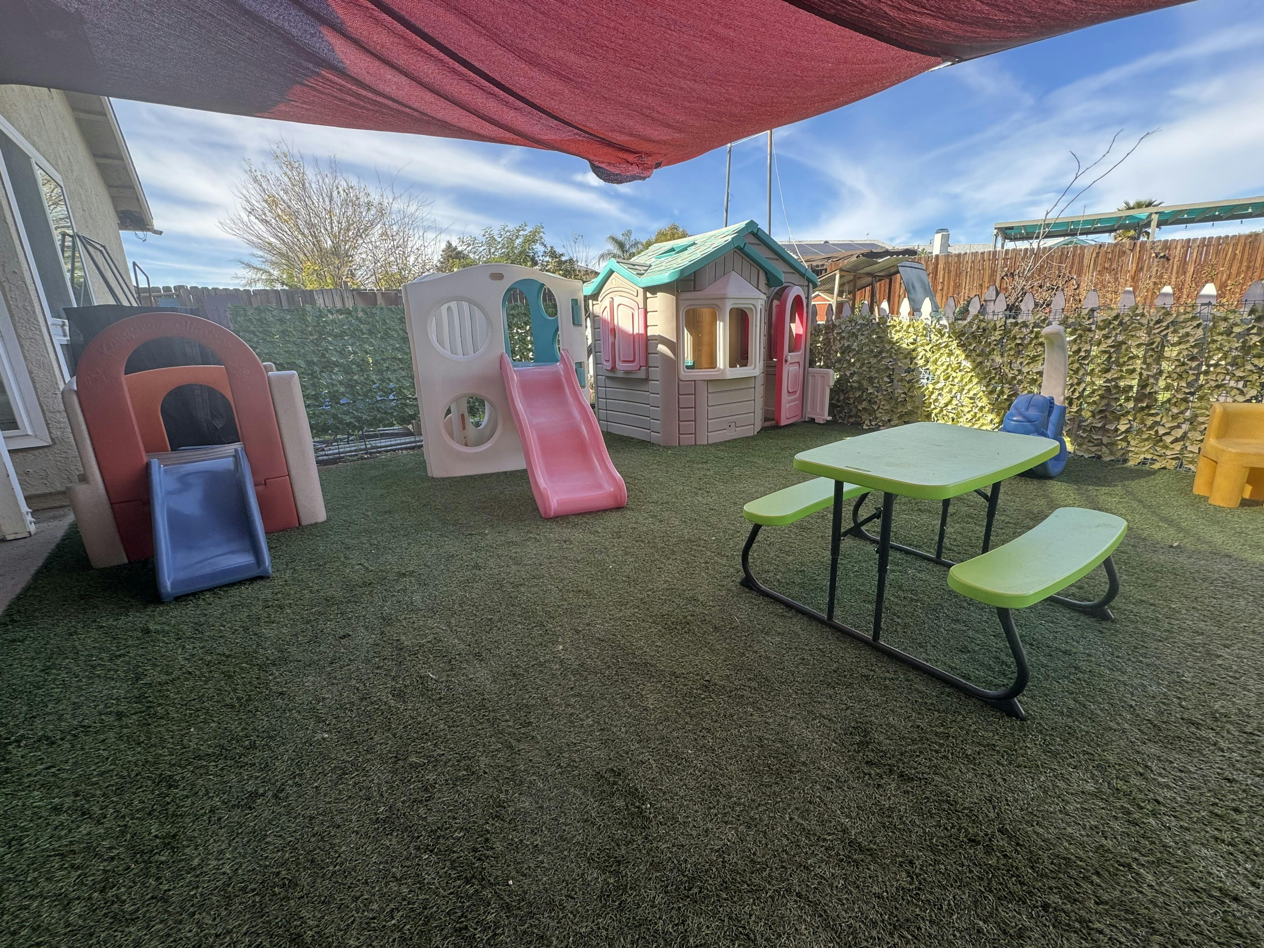 Playground with several plastic play structures, slides, and a picnic table on artificial turf
