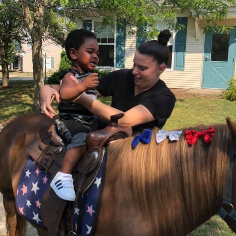 Person helping a child sit on a pony