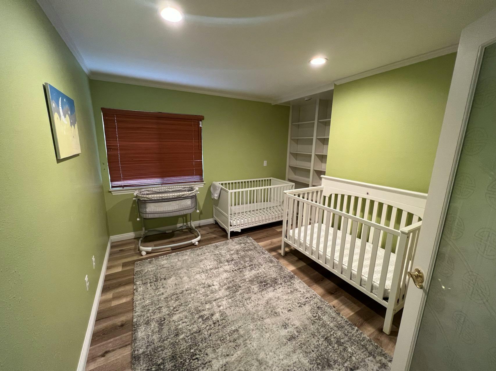 Two white cribs and a changing table in a room with green walls