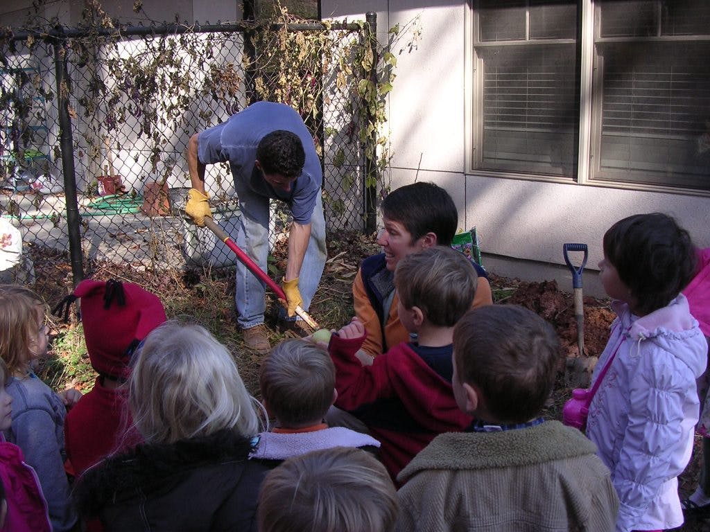 Adult digging with a shovel while children watch