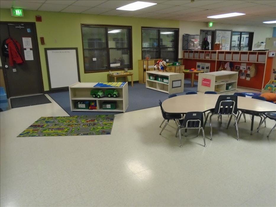 Classroom with child-sized tables and chairs, shelves, and a playmat on the floor