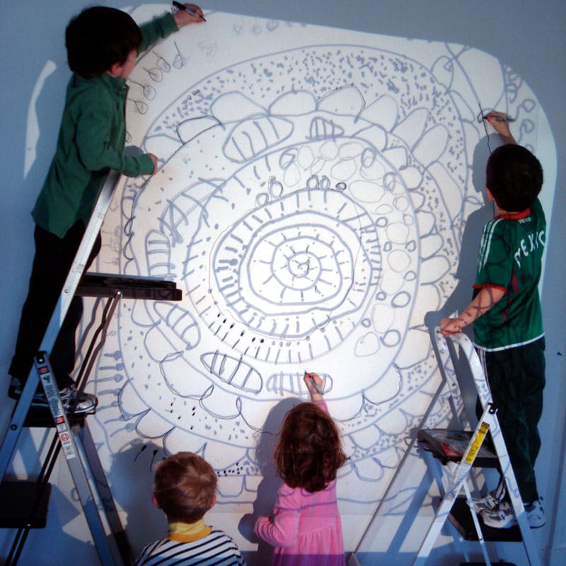 Children drawing on a large white surface with a projected image