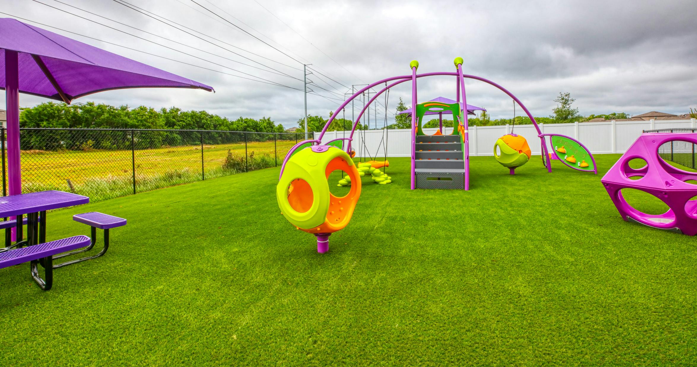 Playground with purple umbrella and colorful equipment on green turf