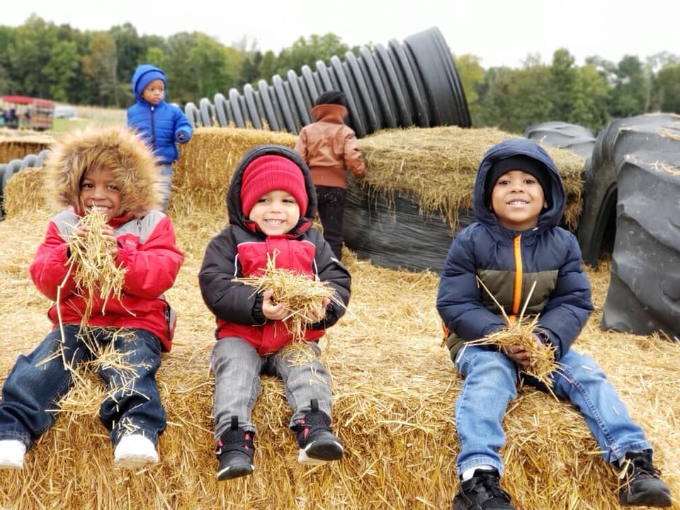 Three children sitting on hay bales holding hay