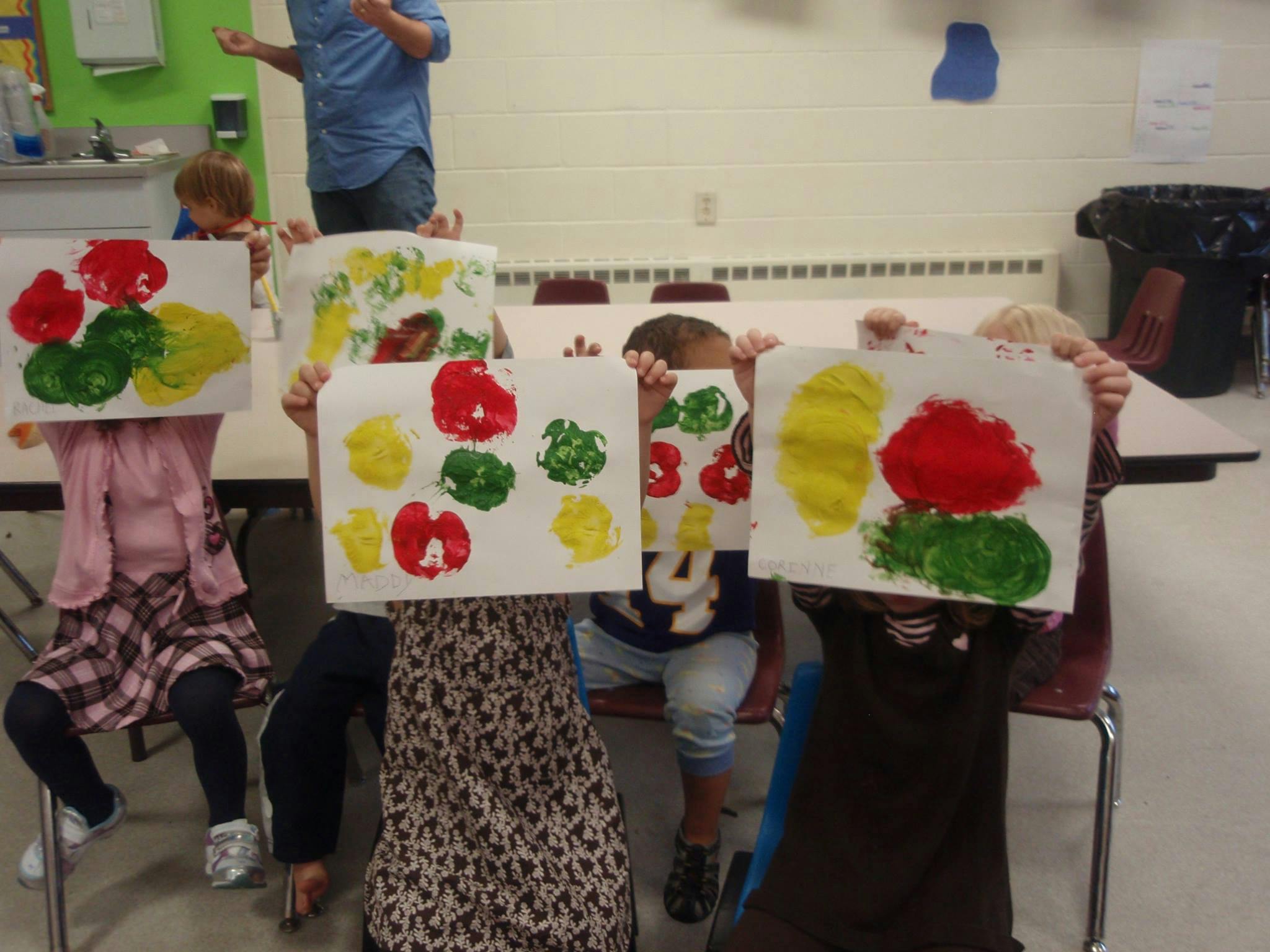 Children holding up paintings with red, yellow, and green shapes