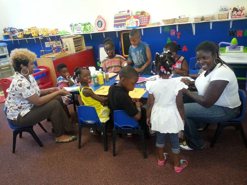 Two adults and multiple children sitting at tables in a classroom